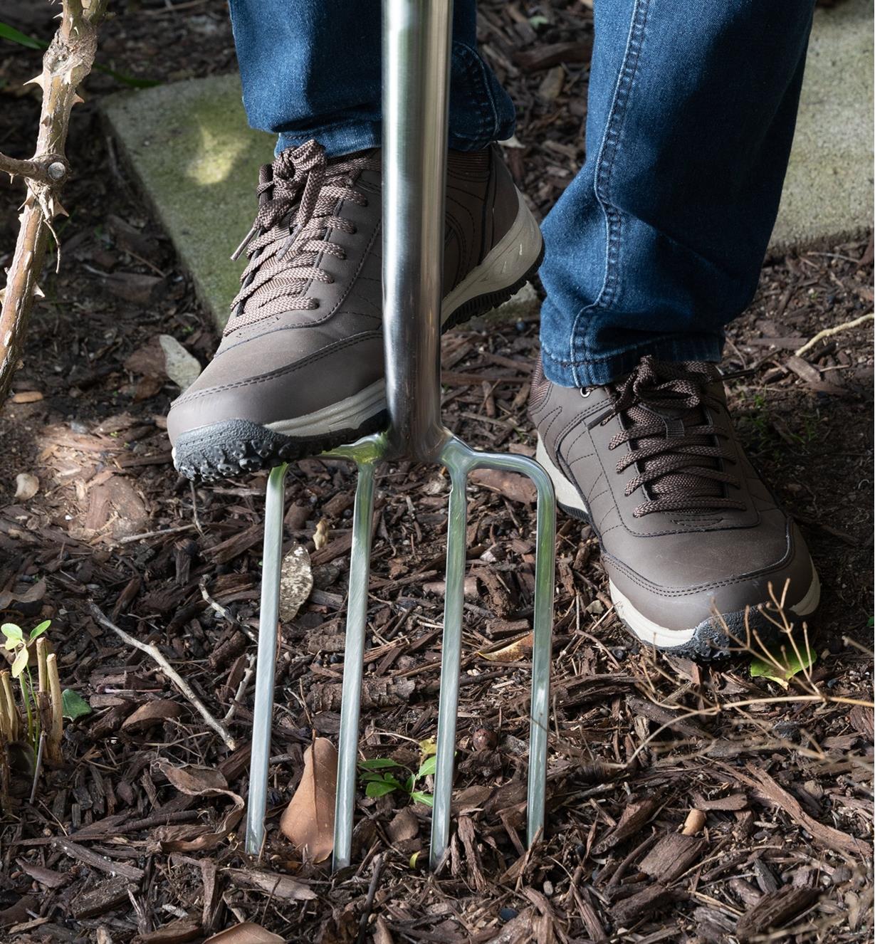 A gardener uses their foot to push the head of the border fork into the ground