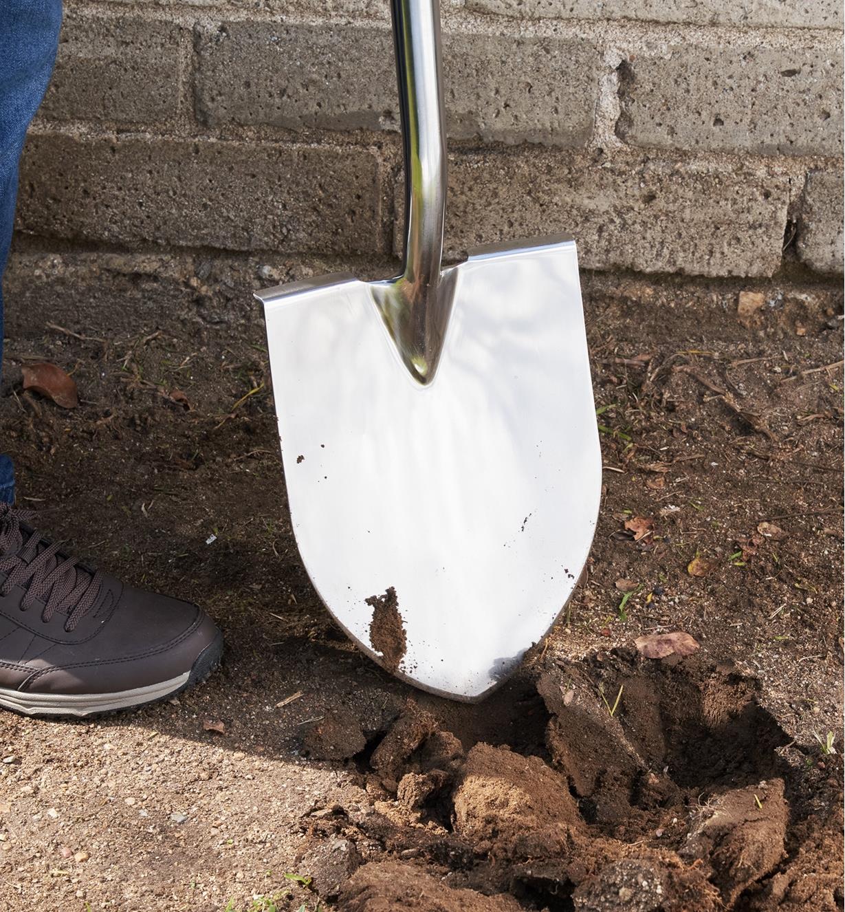 The head on the stainless-steel shovel next to a hole in the ground