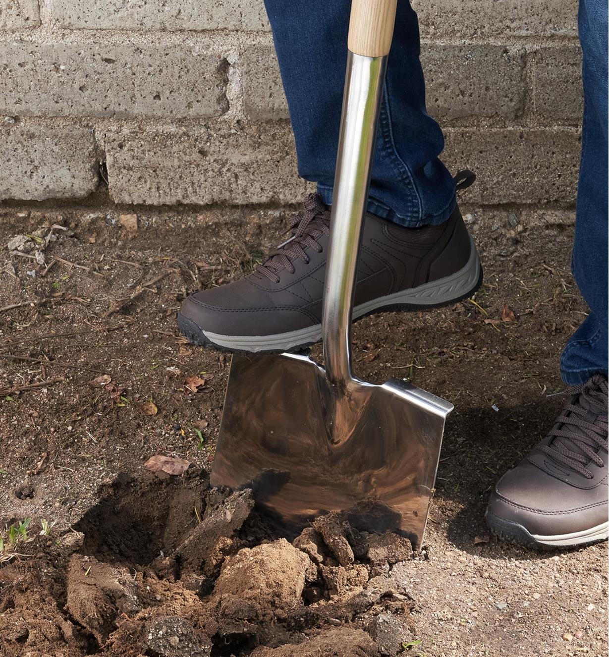 A gardener uses their foot on a foot tread to push the stainless-steel shovel into the ground