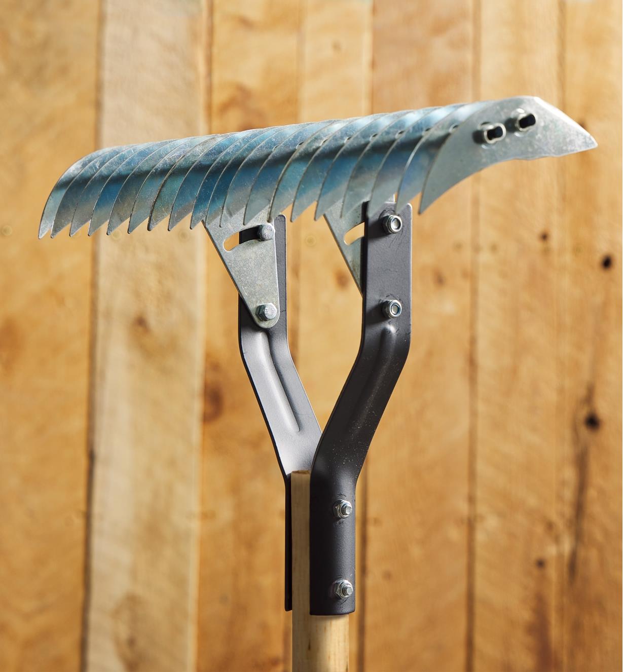 A thatch rake stands upright in front of a wooden background 