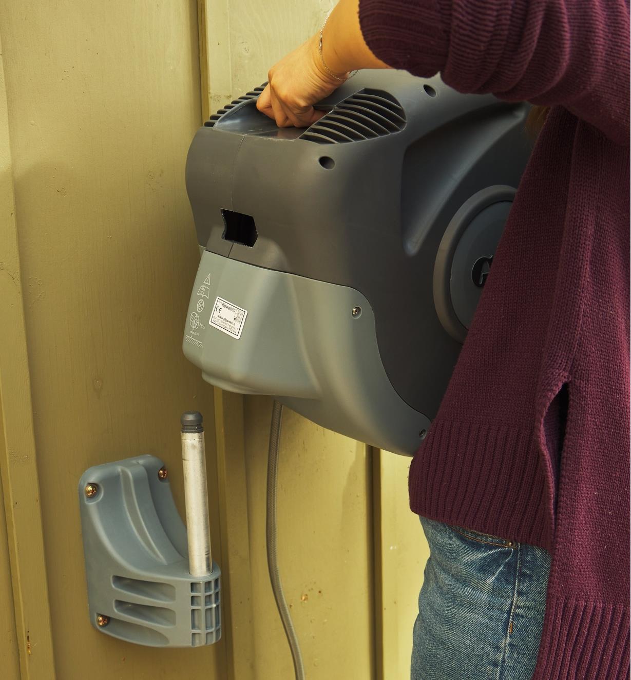 A woman mounts the auto-retracting hose reel to a wall