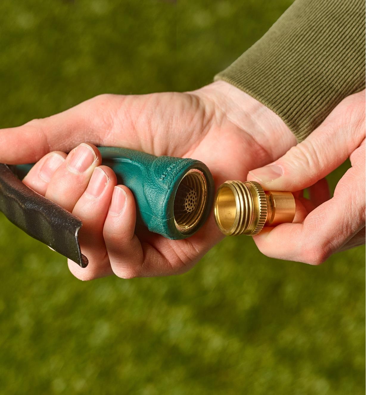 A hose nozzle is held in one hand with a male tool adapter held in the other hand