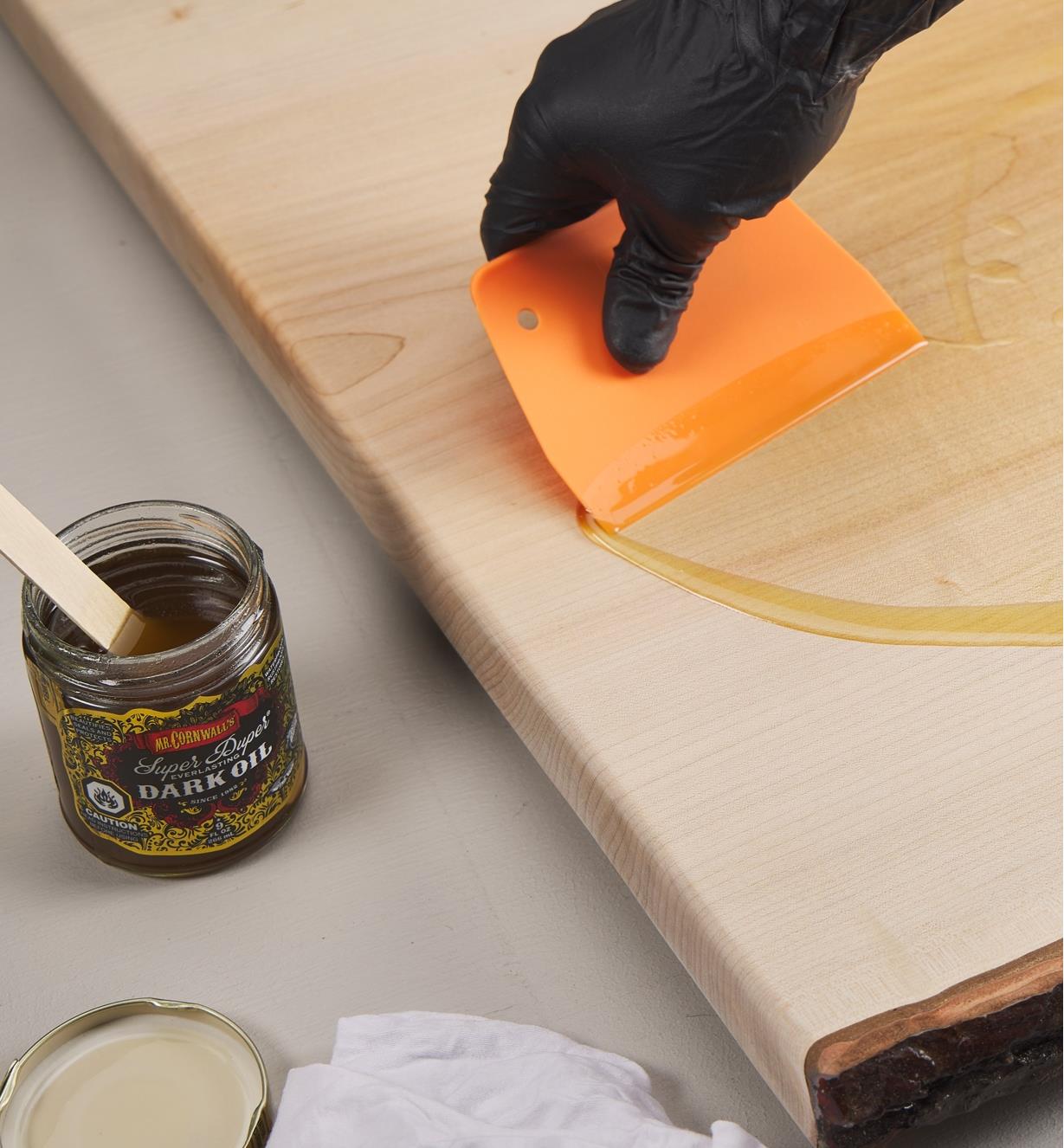 Applying Odie’s dark oil to a wood panel using a spreader