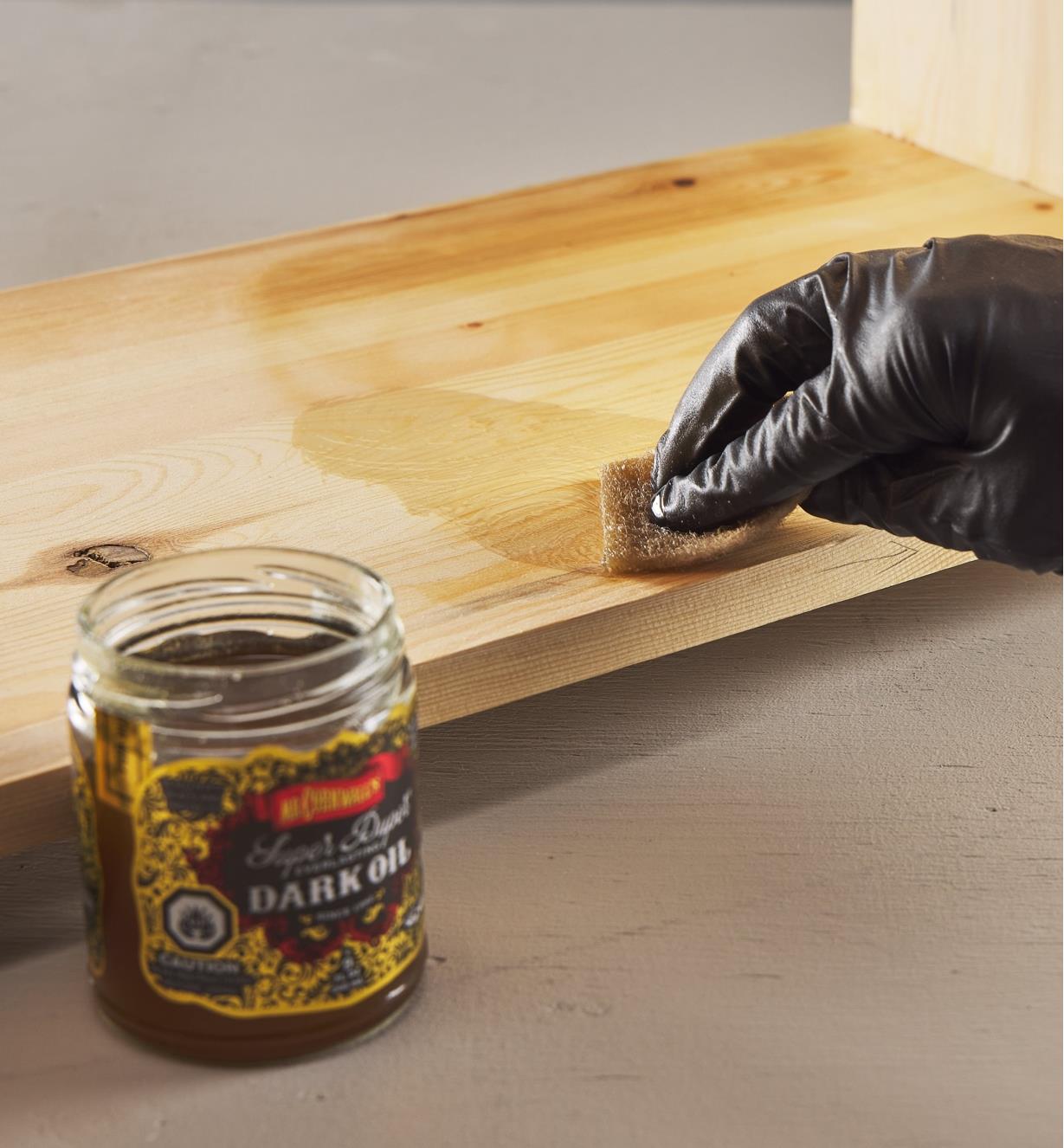 Applying Odie’s dark oil to wood using a sponge