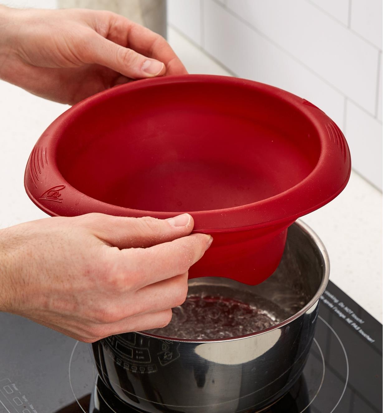 Personne tenant un bol en silicone au-dessus d'une casserole contenant de l'eau bouillante