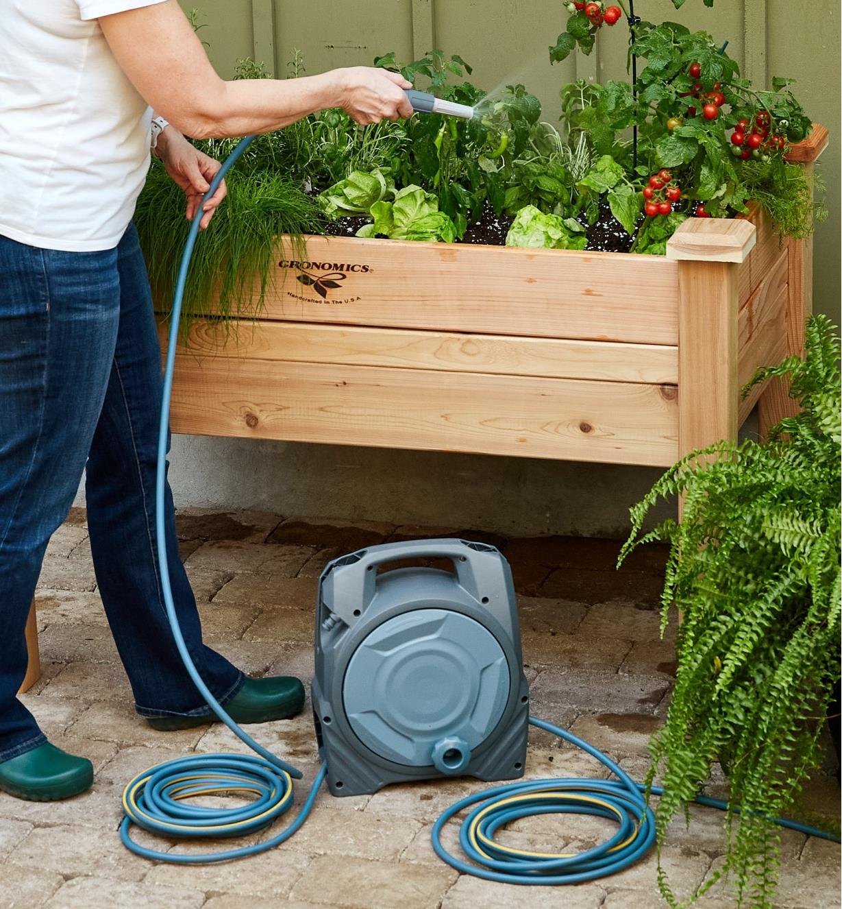 A gardener uses the hose from the manual reel to water vegetables in a raised planter