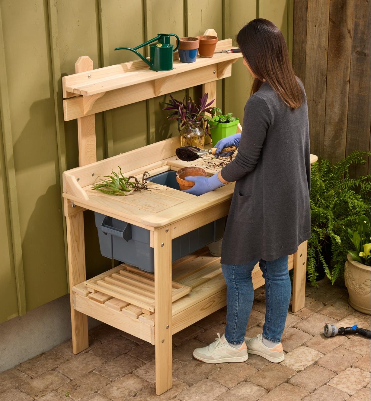 A gardener stands at the cypress potting table while scooping soil into a pot