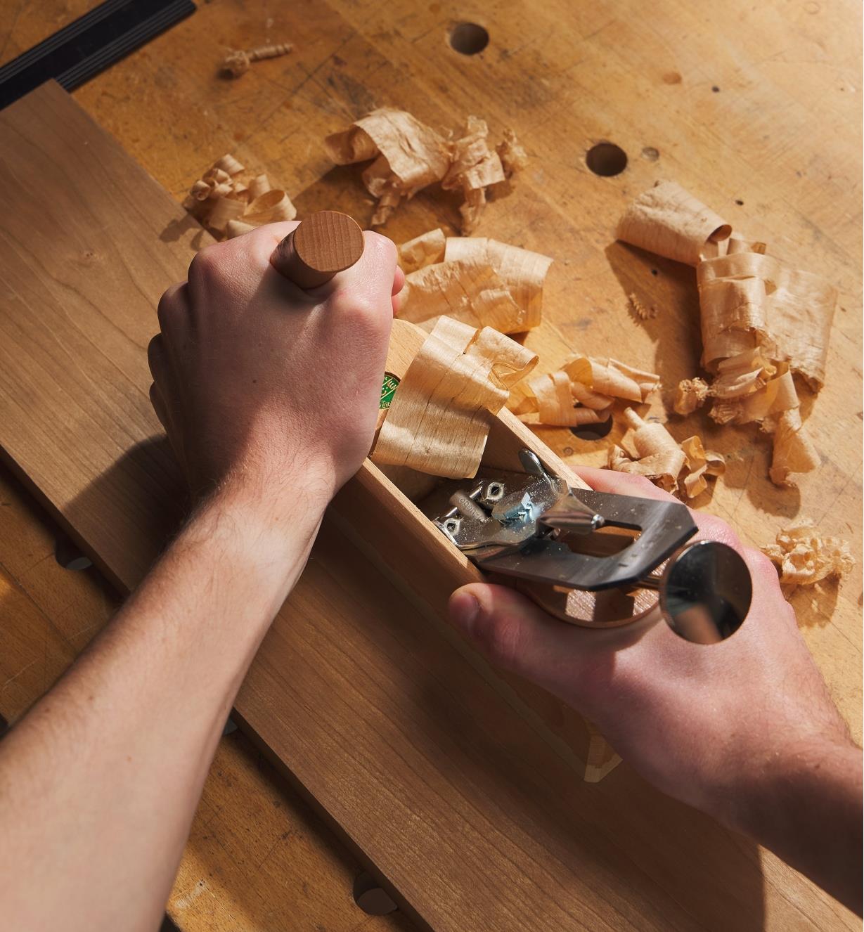 A woodworker using an E.C. Emmerich Primus smooth plane on a cherry-wood board, seen from above