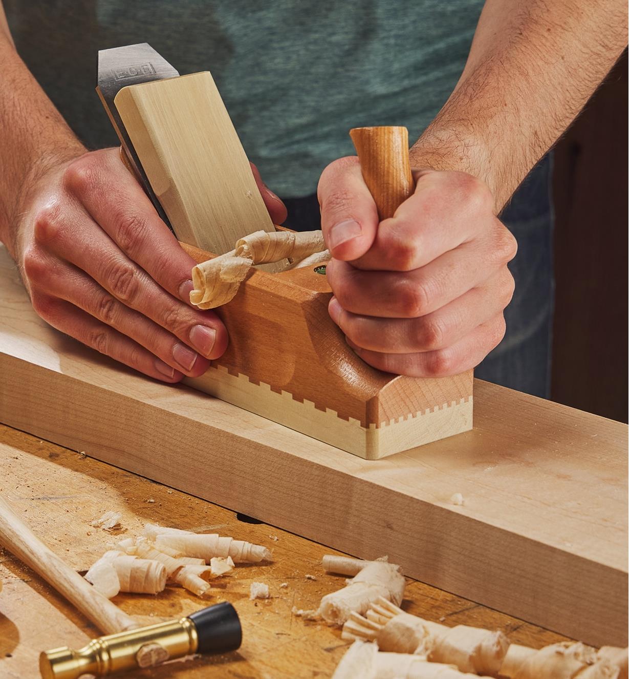 Personne utilisant un rabot à recaler traditionnel en bois E.C. Emmerich pour raboter une planche de cerisier