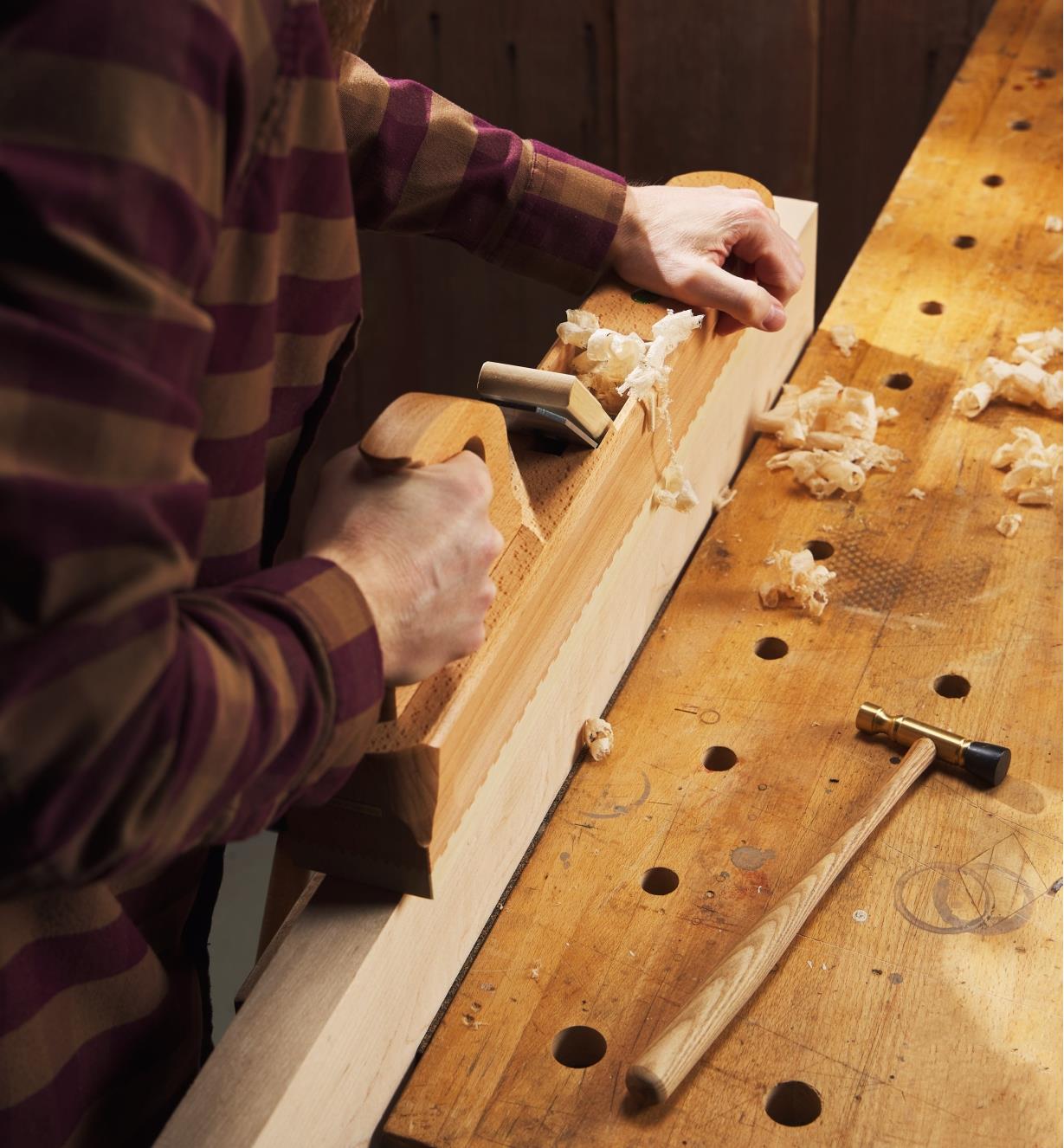 A woodworker edge-jointing a large maple board with an E.C. Emmerich traditional wooden try plane