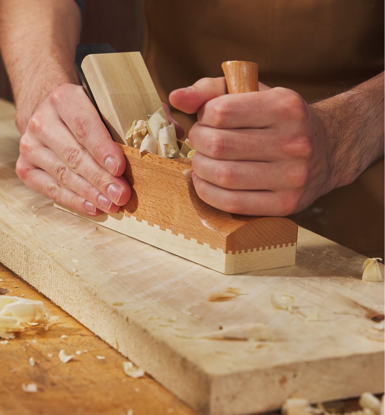 Personne utilisant un riflard traditionnel en bois E.C. Emmerich pour raboter une large planche de bois brut