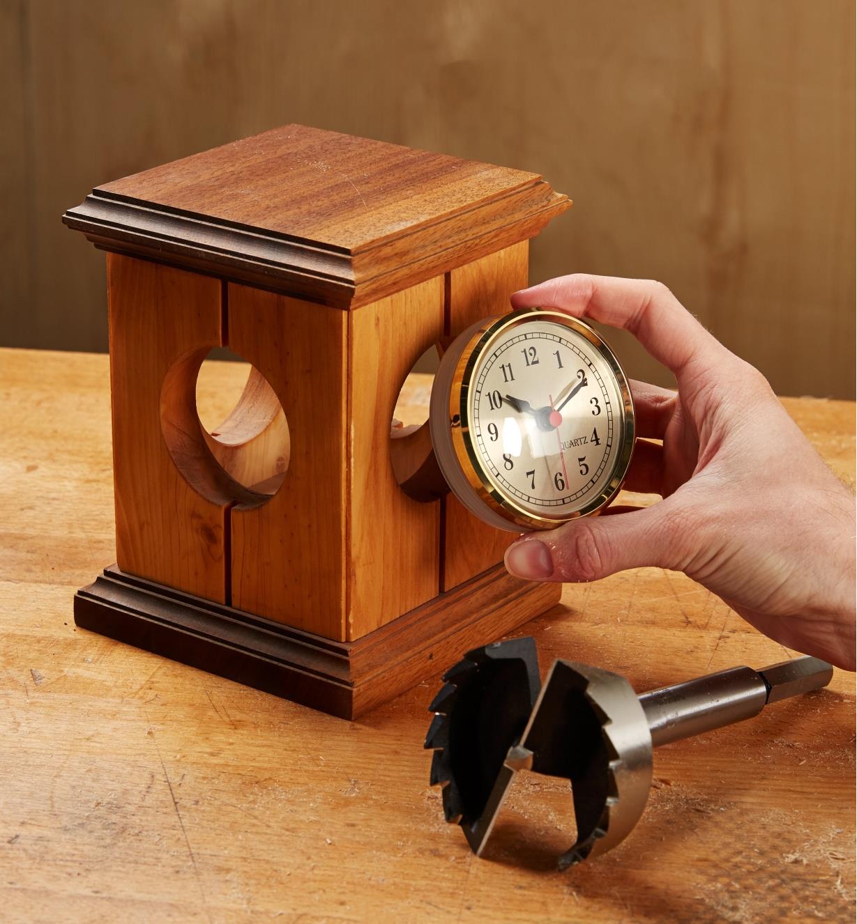 Fitting the Arabic numeral model of the clock insert into a wooden framework, with a Forstner drill bit lying beside it