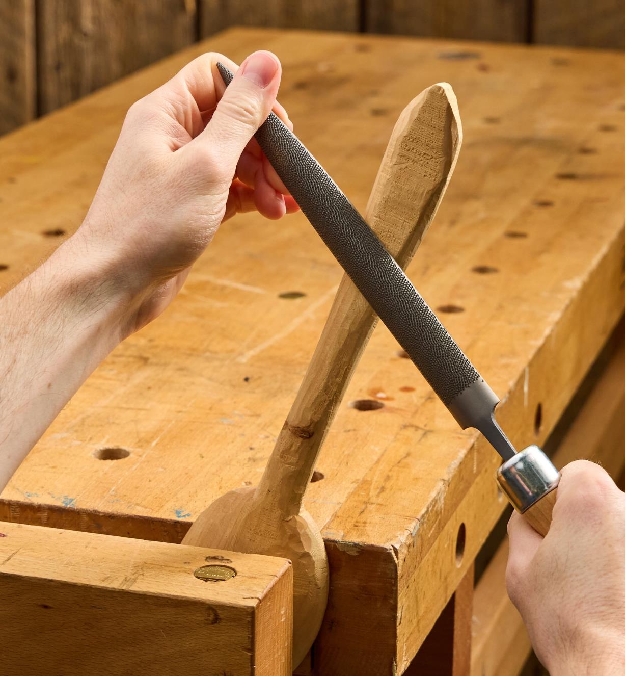 Personne utilisant une râpe demi-ronde Corradi pour façonner le manche d'une cuillère en bois