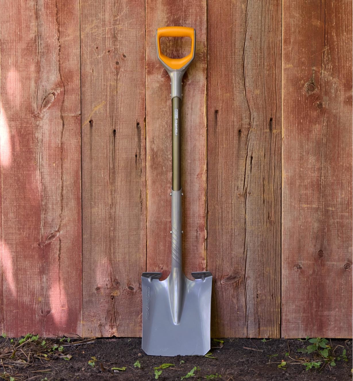 A Fiskars transfer shovel with an orange handle leaning against fence boards