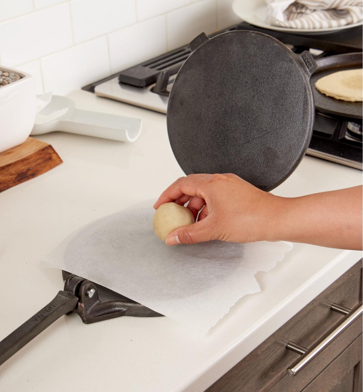 Placing a ball of dough onto a piece of parchment paper that is lining the tortilla press