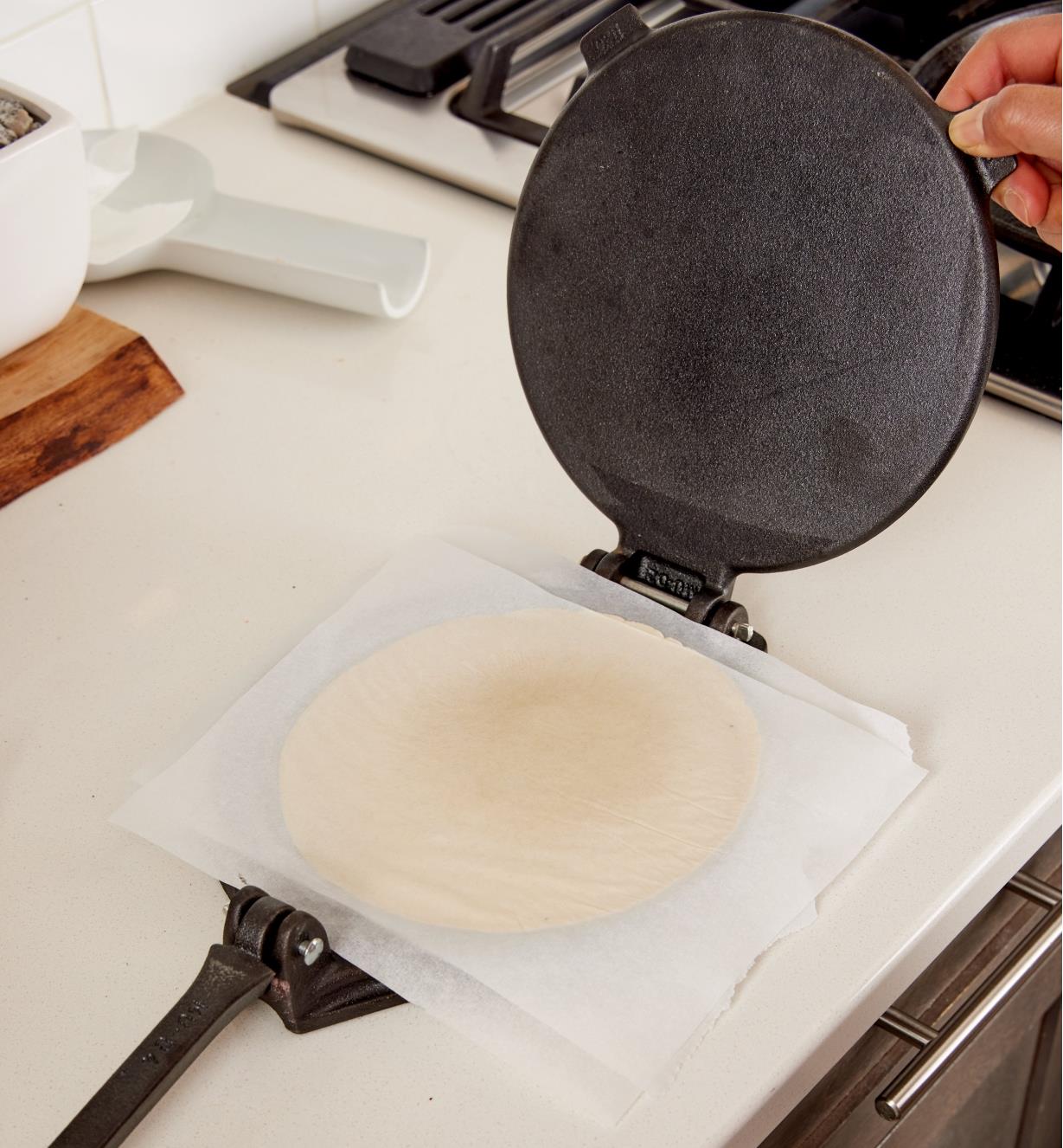 Personne relevant la plaque supérieure d'une presse à tortilla pour révéler une tortilla entre deux feuilles de papier parchemin sur la plaque inférieure