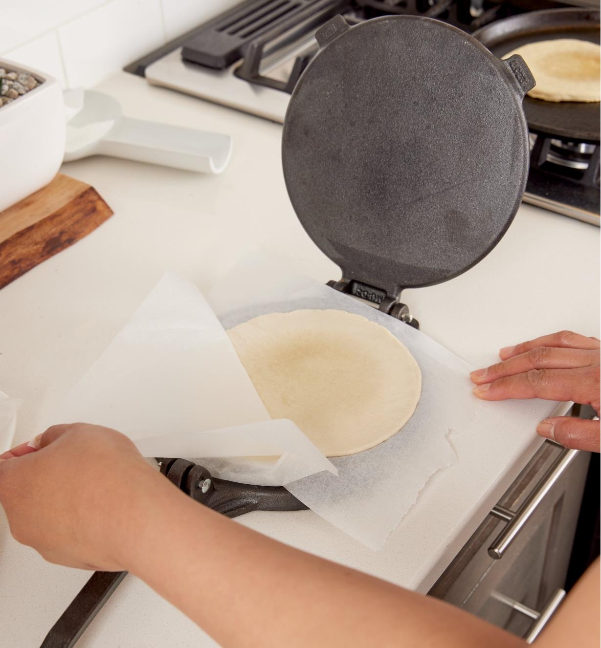 Lifting a piece of parchment paper off of a tortilla on the tortilla press