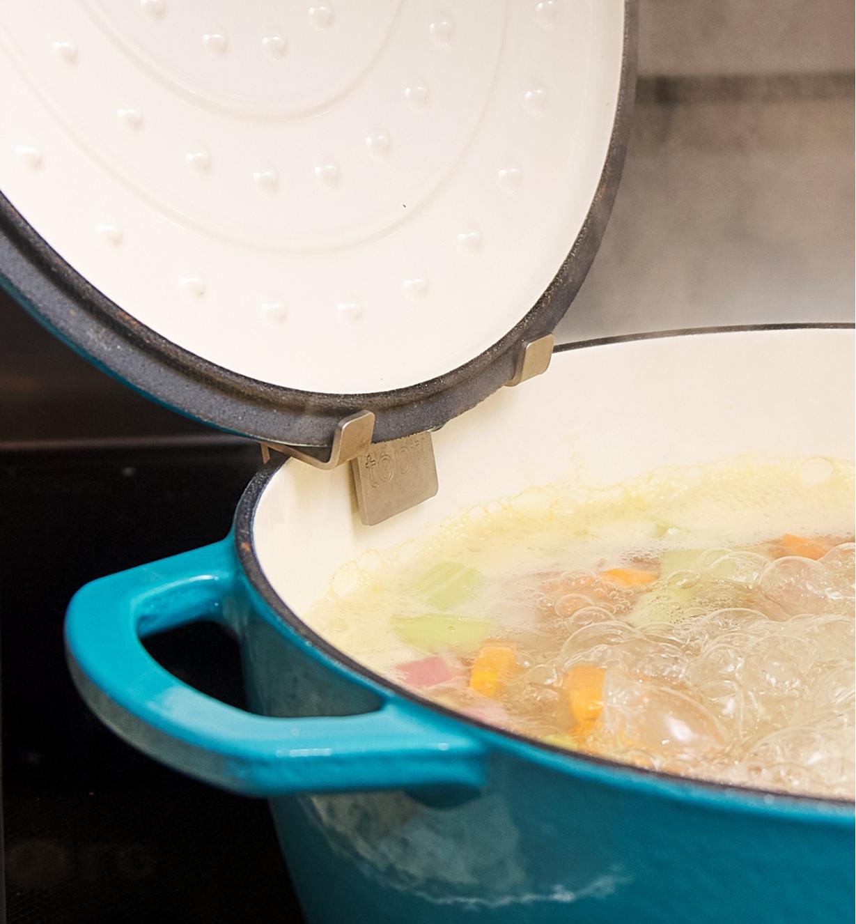 Soupe frémissant dans une cocotte, le couvercle reposant sur un support en inox accroché sur la paroi