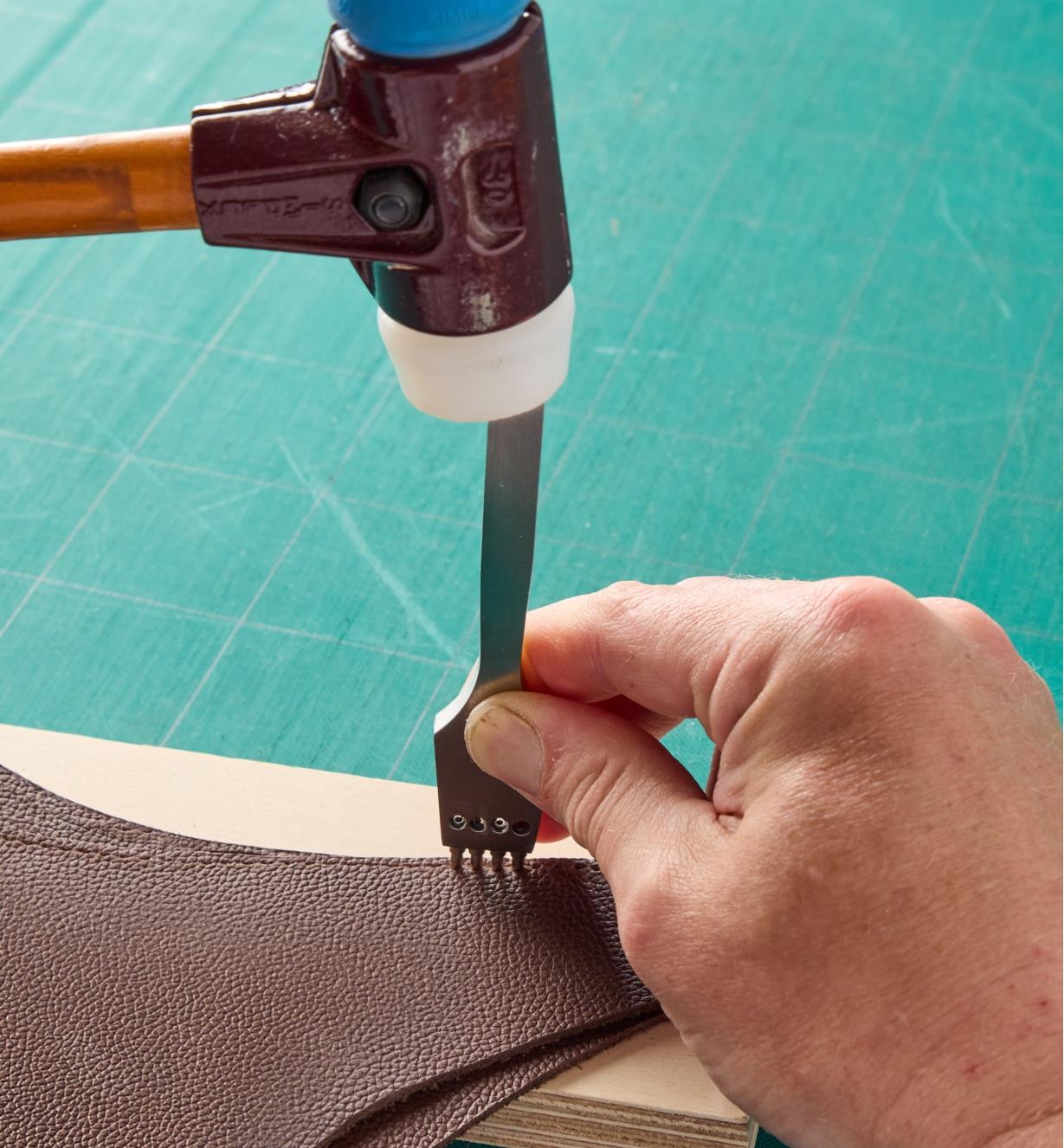 Using a mallet and a four-prong tube punch to punch holes in a piece of leather