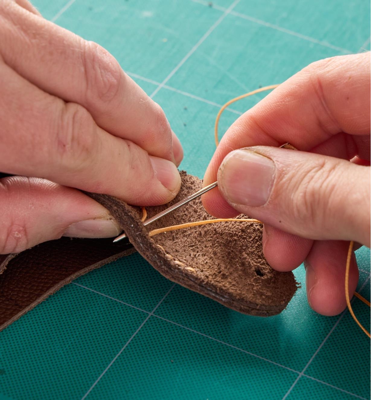 Using a needle and thread to stitch a piece of leather