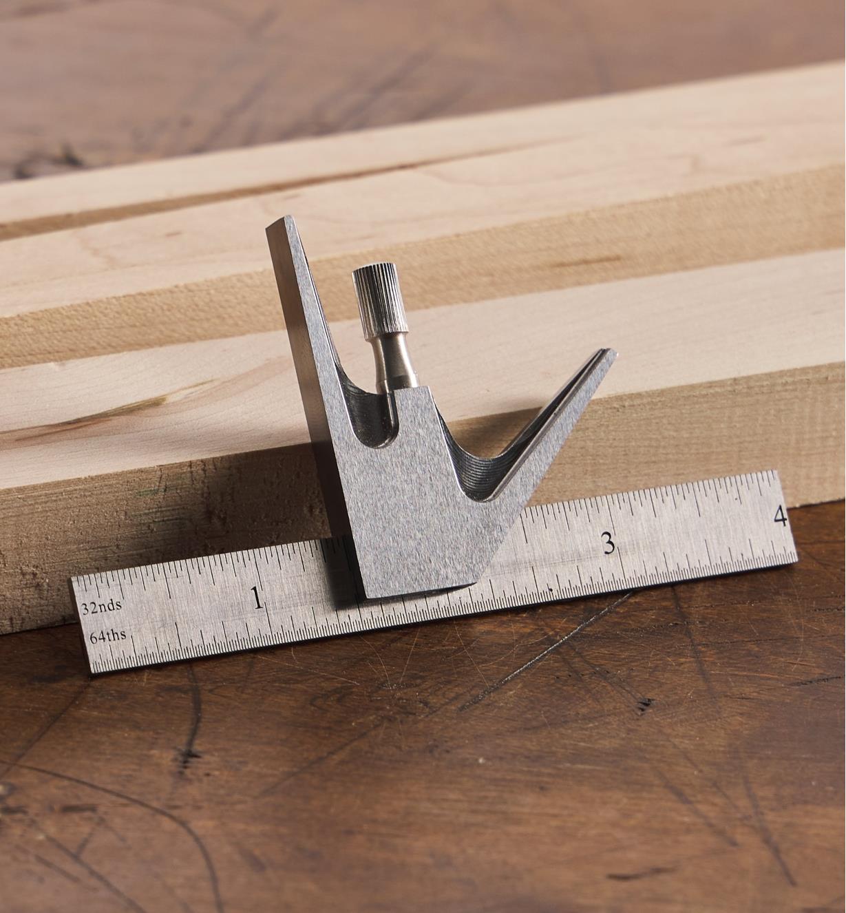 A Lee Valley 4" combination square leaning against a piece of wooden stock on a workbench