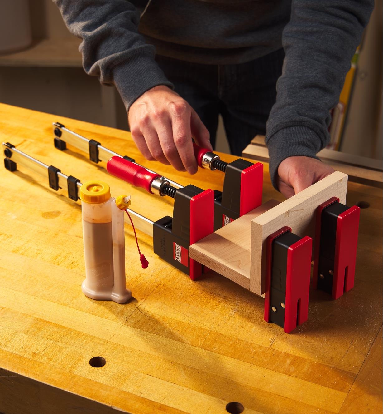 A woodworker uses two Bessey K Body REVO JR clamps to hold a wooden assembly together during glue-up