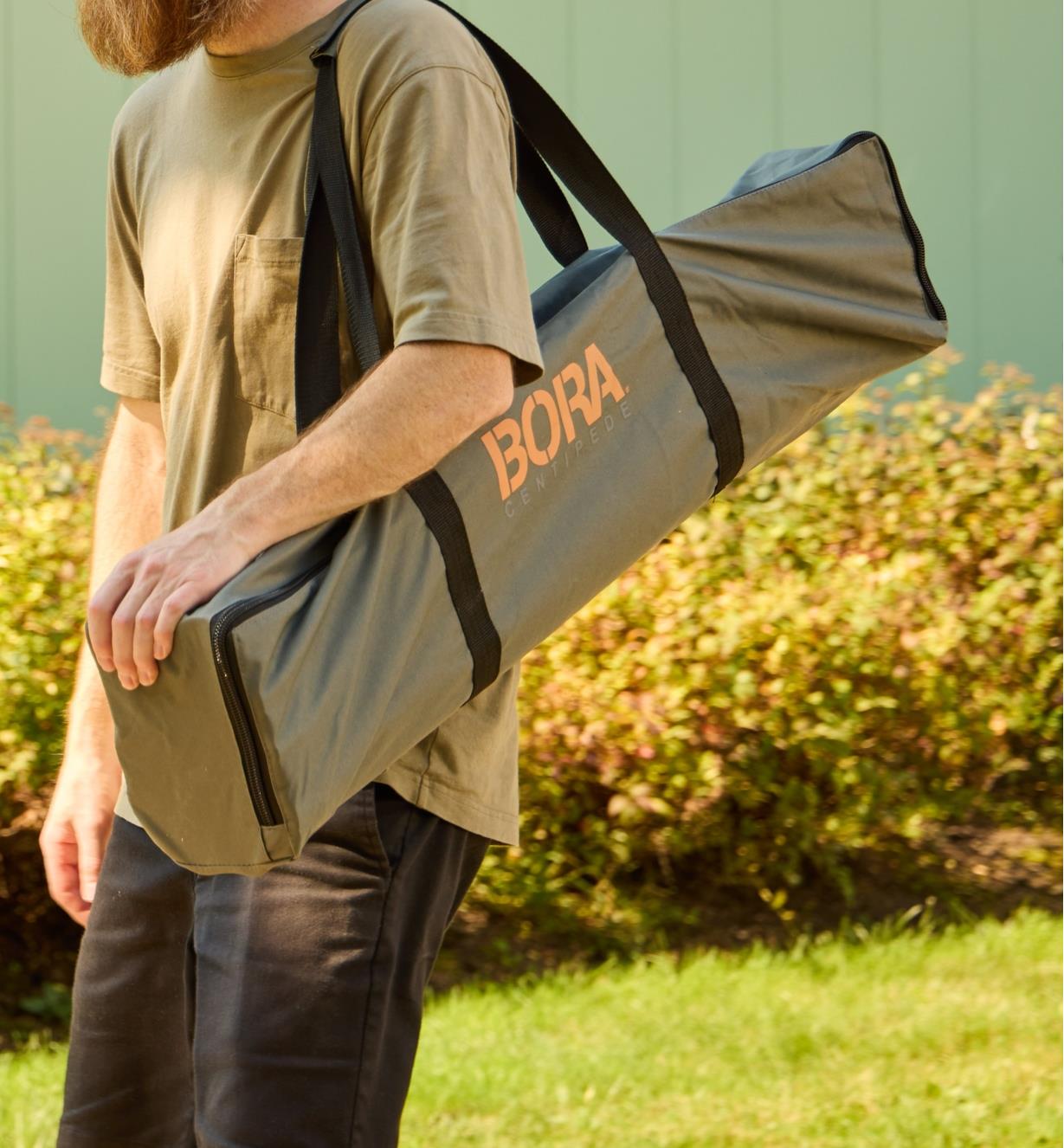 A man carries a folded Bora Centipede table bundled inside a nylon tote