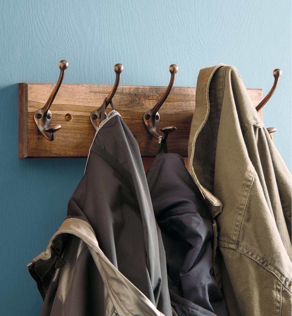 Five double hooks on a board attached to a wall, with three jackets hanging from them