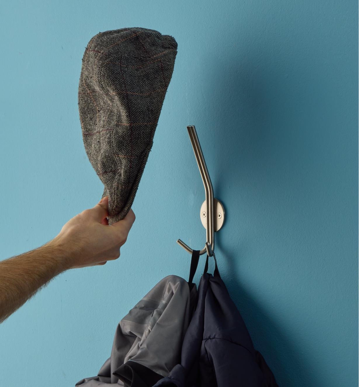 A cloth hat being placed on the top hook of a stainless-steel triple hook