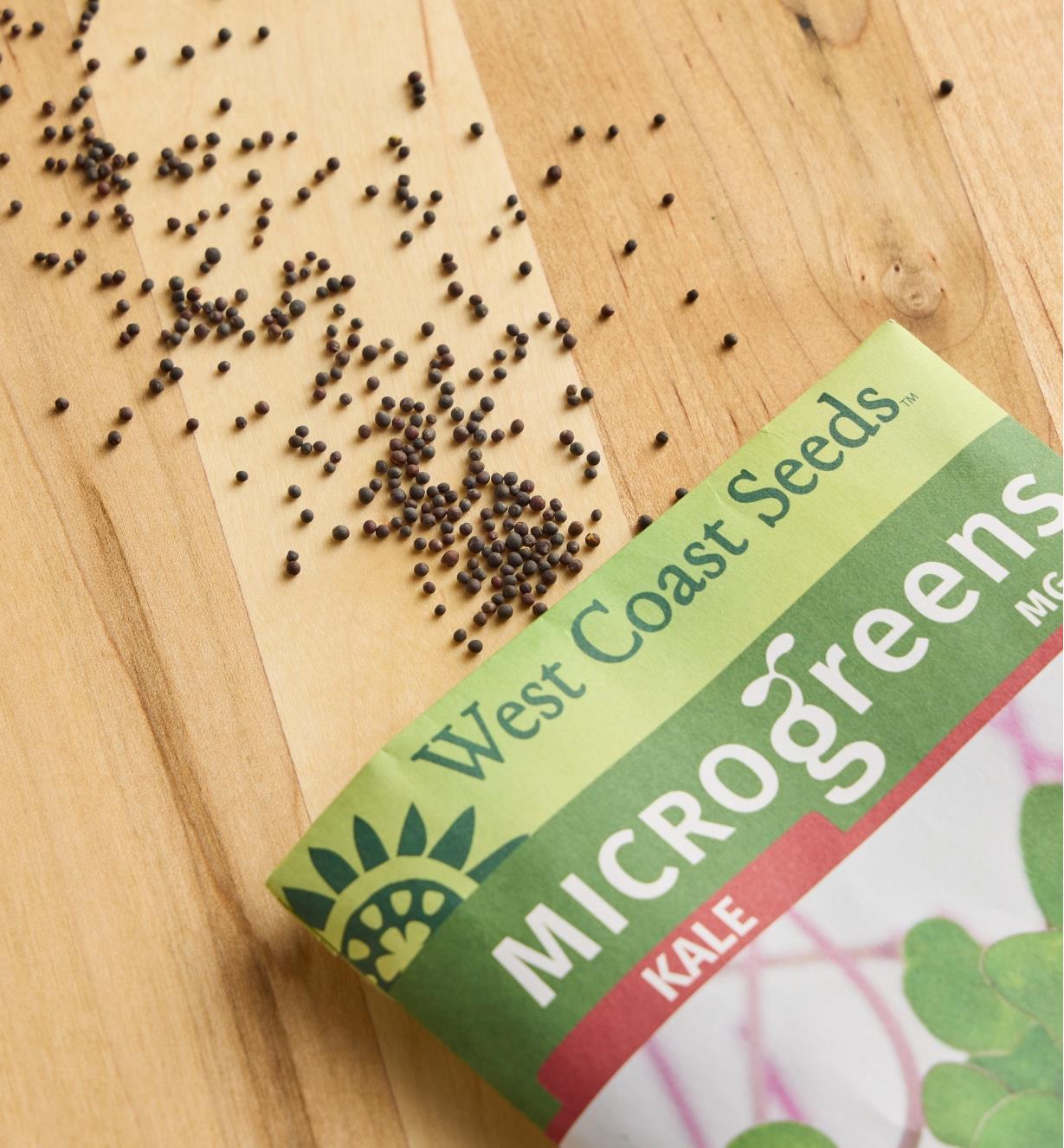 Kale microgreen seeds spread out on a wood surface next to a seed packet