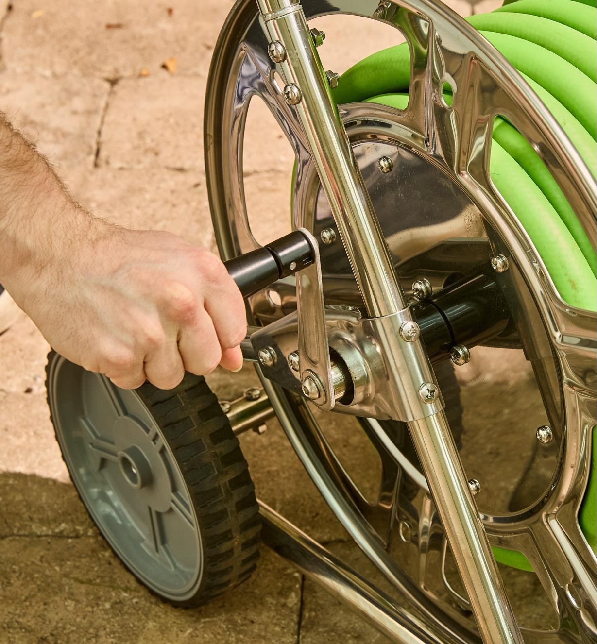 Personne tournant la manivelle d'un dévidoir pour boyau d'arrosage sur chariot en acier inoxydable